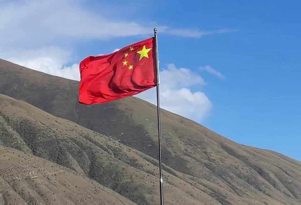 China travel tips article. The Chinese flag fluttering against a background of blue sky with fluffy clouds and a rural hillside