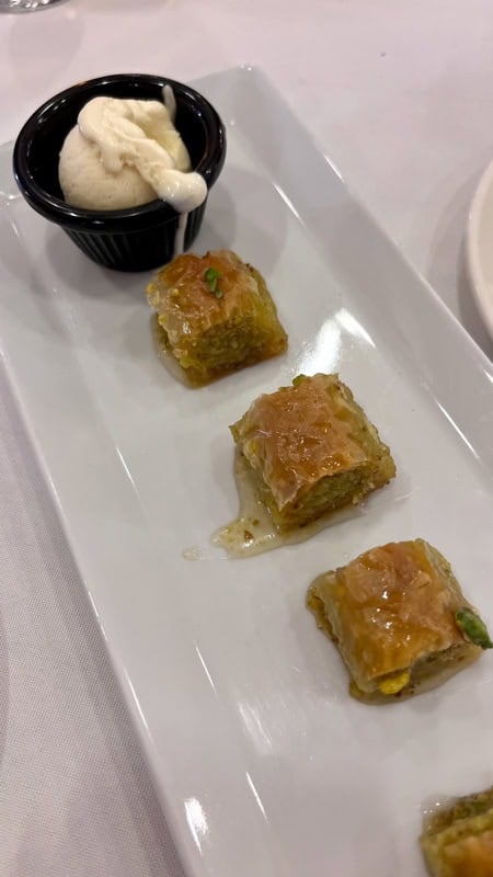 Small pieces of baclava on a rectangle dish served with a small ramekin of vanilla ice cream
