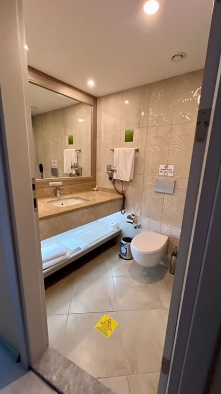 A well-lit, modern bathroom featuring a marble vanity, white toilet, and a wet floor warning sign on tiled floor.