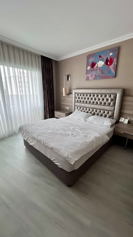 A modern hotel room with a large bed, tufted headboard, and a colorful floral painting.