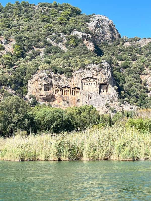 View of the Lycian Rock Tombs of Dalyan, Turkey, carved into a lush cliff face above the Dalyan River.