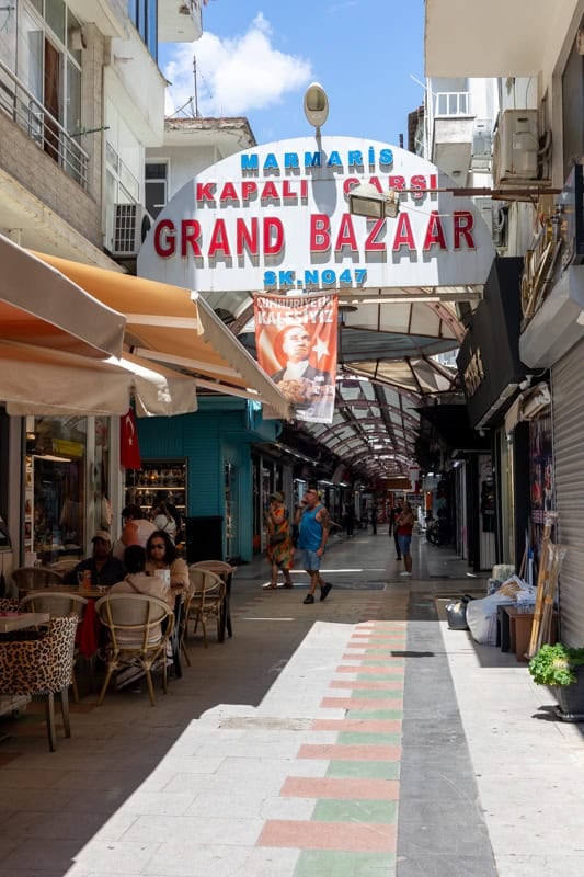 The entrance to the Grand Bazaar in Marmaris. People sit under awnings at table and chairs drinking coffee