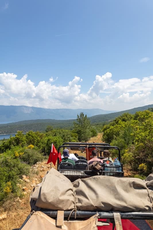 Off-road vehicle with a Turkish flag driving through scenic coastal mountains and sea in Turkey.