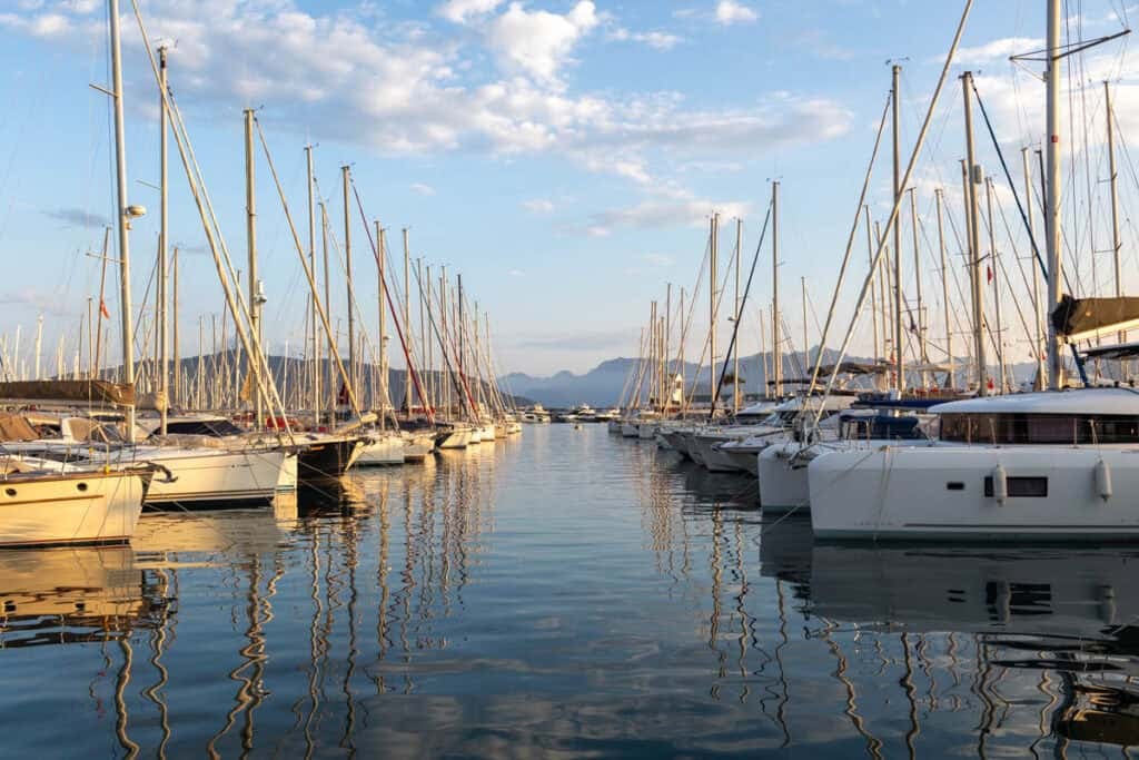 A serene marina filled with numerous sailboats and yachts, with rugged mountains under a partly cloudy sky.