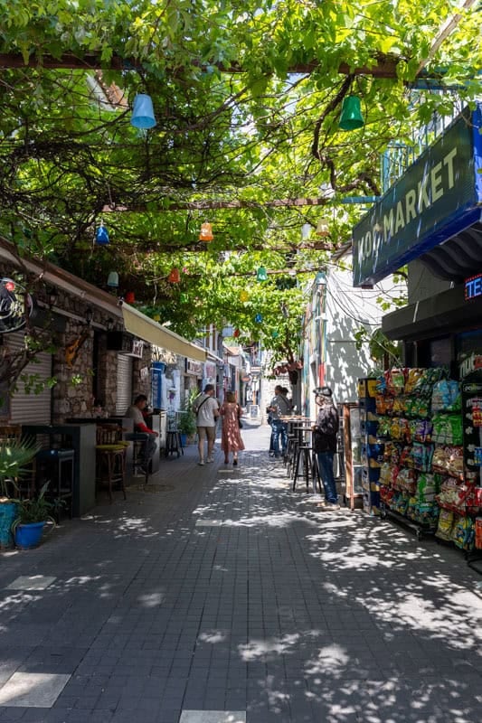 People walk past stalls in Marmaris old town. A canopy of green foliage shelters them from the sun
