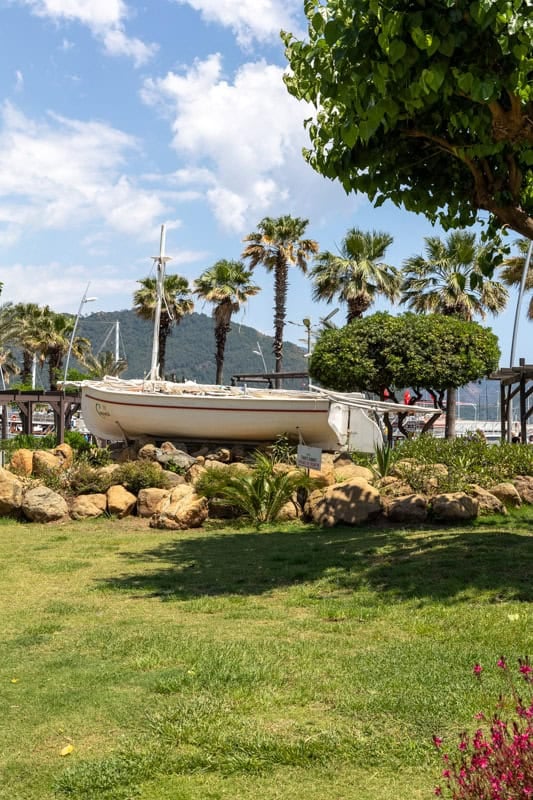 A small white boat sits on rocks in a small park on Marmaris seafront