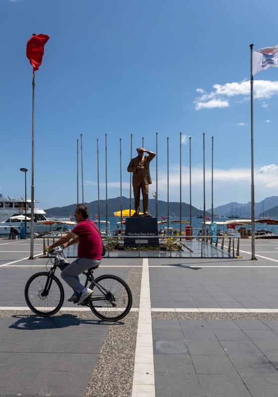 A man in a red shirt cycles past an Attaturk statue on Marmaris seafront