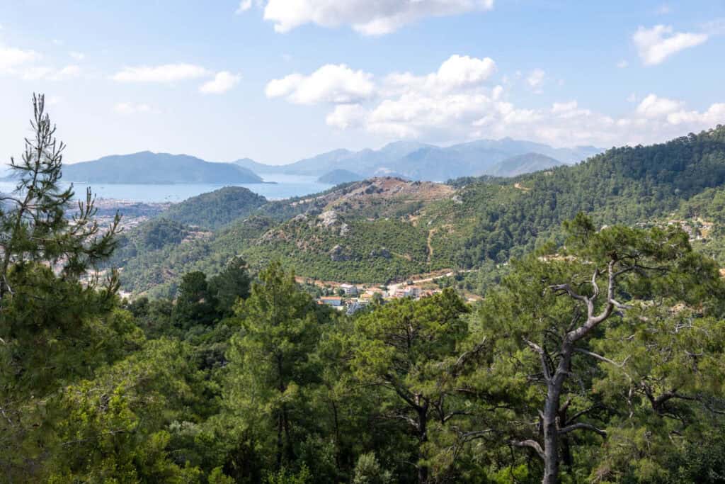 Panoramic view of Marmaris Bay, Turkey, with forested hills, a coastal town, and distant mountains under a blue sky.