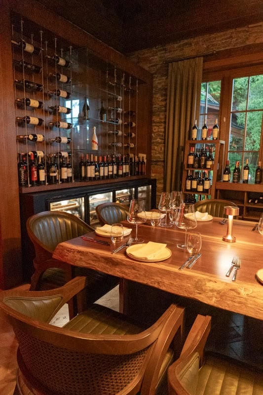 Sento by NUUP restaurant in Marmaris. A dining table made from a slab of thick wood is set for dinner with a display of wine behind